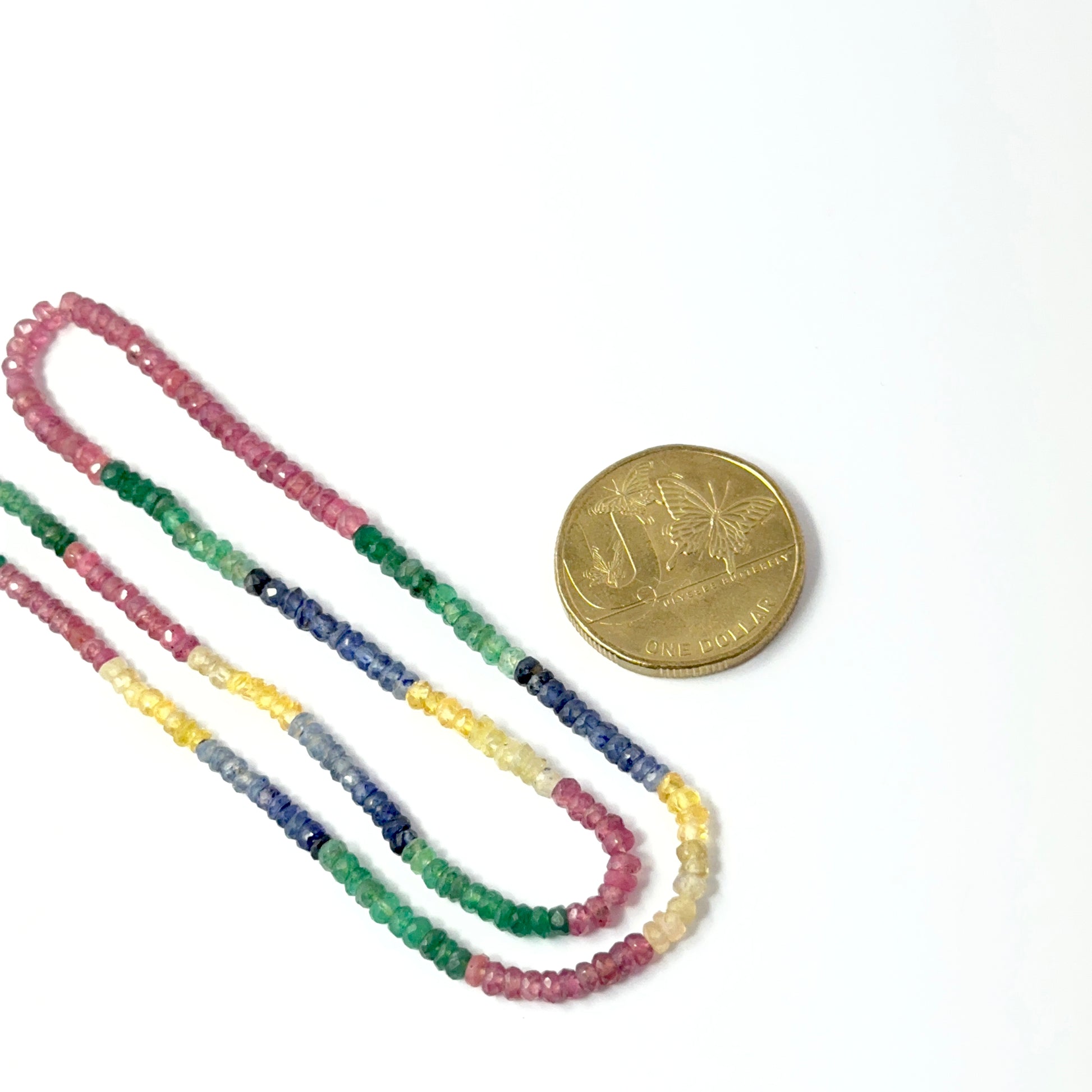 A coin is place near delicate strands of multi precious gemstone beads for scale