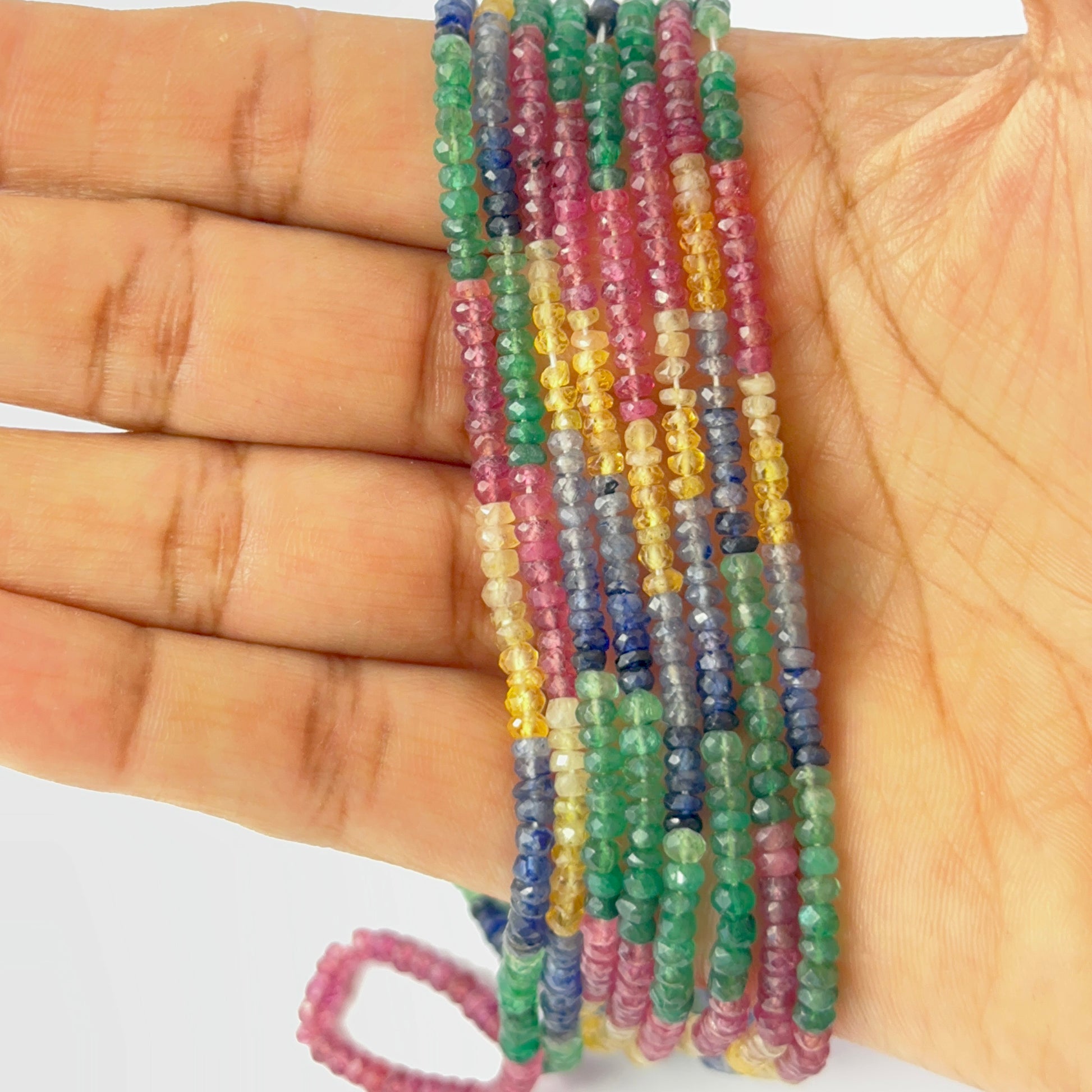 A person holds delicate strands of multi precious gemstone beads, showcasing their faceted rondelle design.