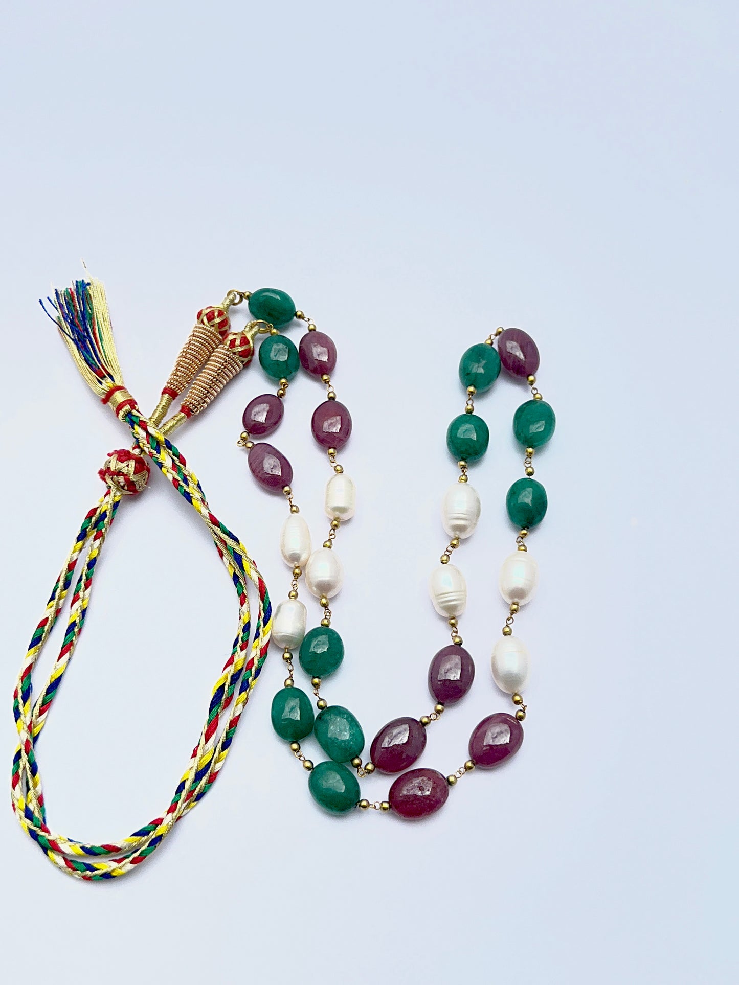 Gemstone necklace with ruby, emerald and pearl beads arranged in a refined layout.