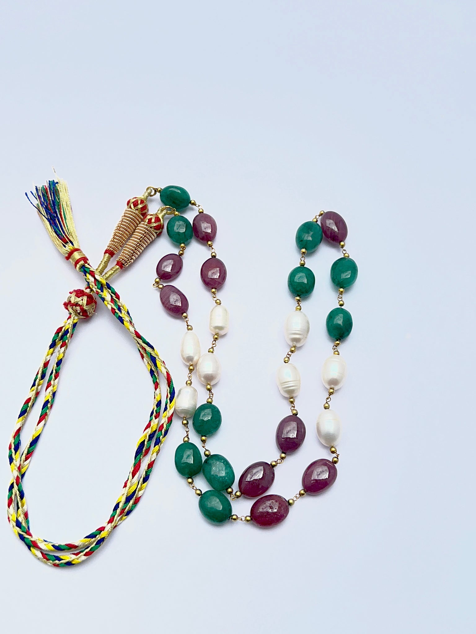 Gemstone necklace with ruby, emerald and pearl beads arranged in a refined layout.