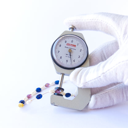 A dial gauge measures the multi precious smooth oval 4.5–5.7mm gemstone.