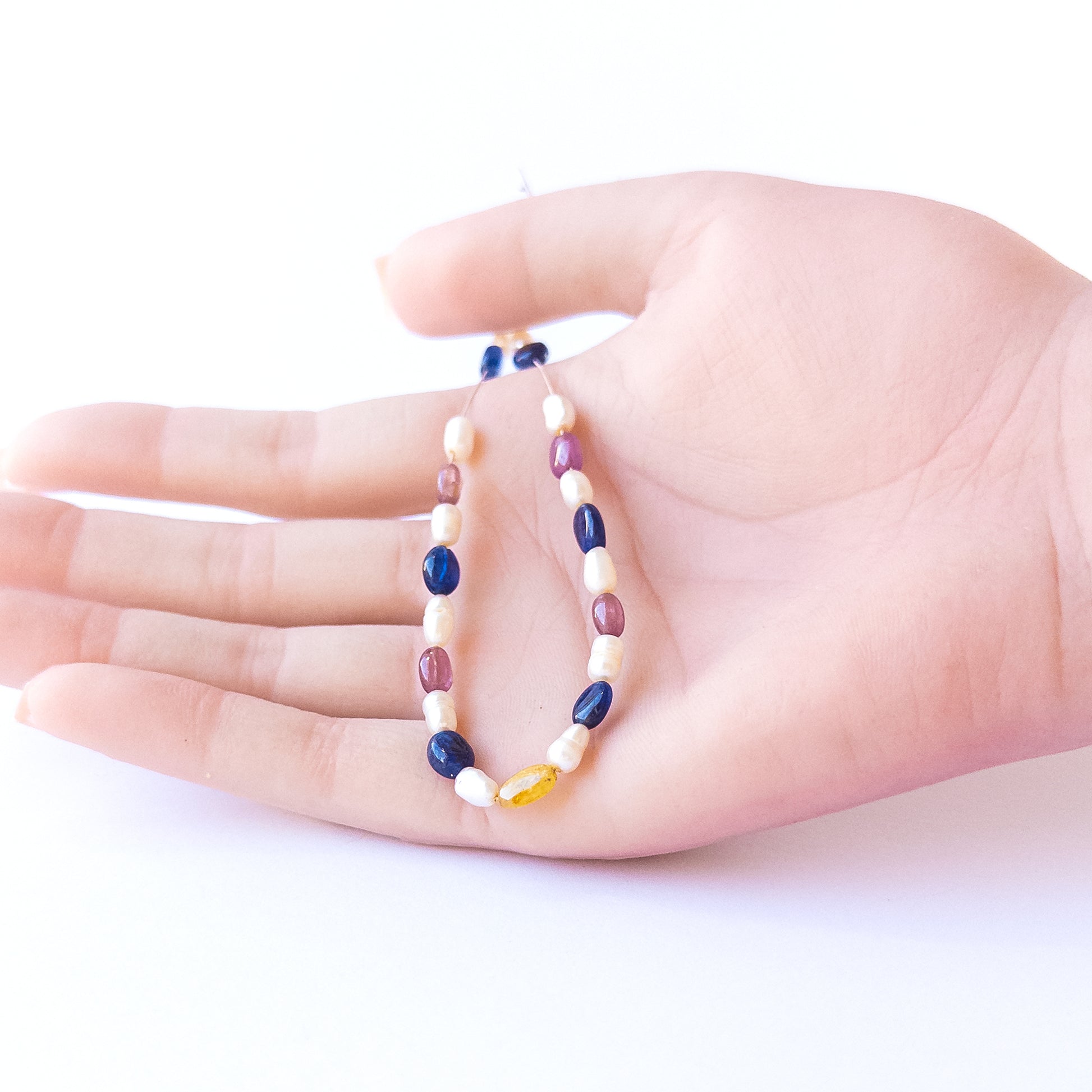 A person holds delicate strands of multi precious and freshwater pearl beads, showcasing their smooth oval design.