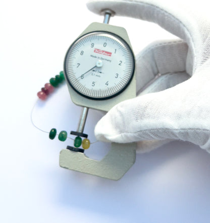 A dial gauge measures the multi-precious rondelle 6.2–6.7mm gemstone.