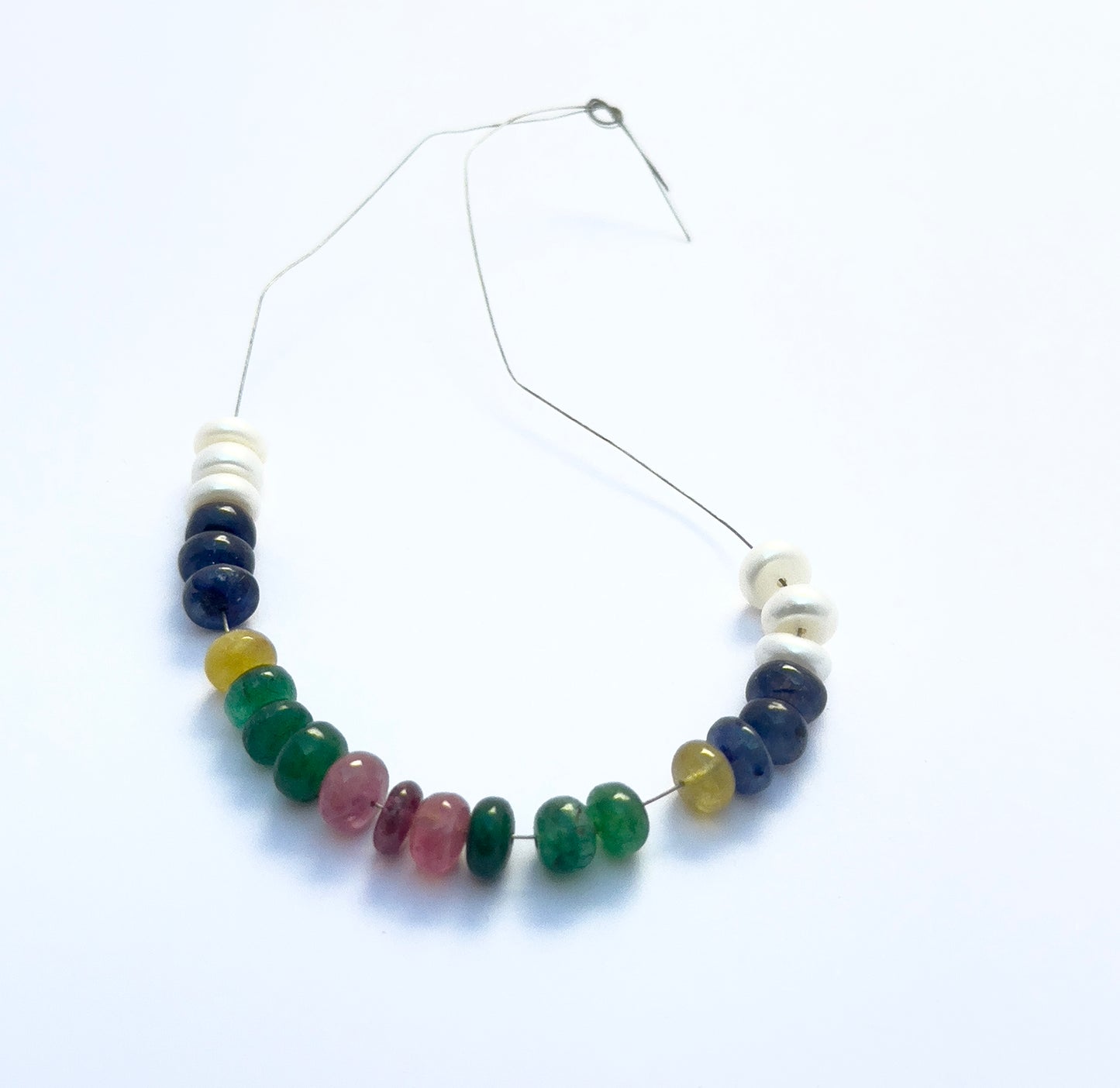 Close-up of natural gemstone beads featuring ruby, emerald, yellow sapphire, blue sapphire, and pearls. 