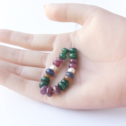 A person holds delicate strands of multi precious and freshwater pearl beads, showcasing their smooth rondelle design.