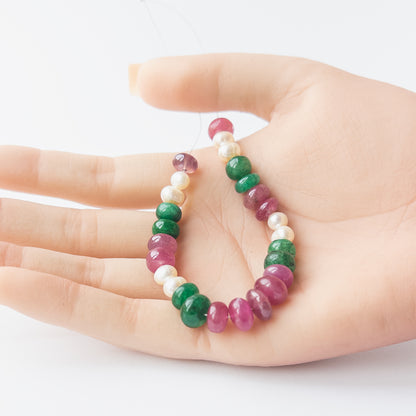 A person holds delicate strands of multi precious and freshwater pearl beads, showcasing their smooth rondelle design.