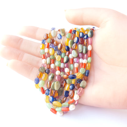 A person holds delicate strands of Multi Precious Navratan beads, showcasing their smooth oval design.  