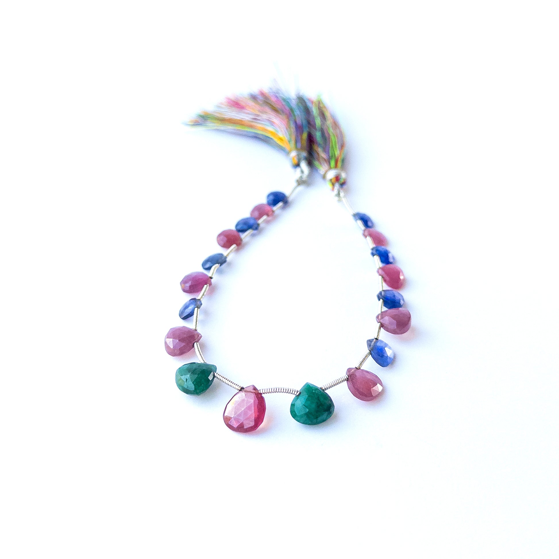 Mixed Ruby, Blue Sapphire and Emerald briolette beads arranged together showing bright gemstone contrast.