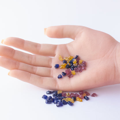 A person holds delicate pieces of Ruby, Blue Sapphire and Yellow Sapphire rough, showcasing their natural design.