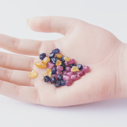 A person holds delicate pieces of Ruby, Blue Sapphire and Yellow Sapphire rough, showcasing their natural design.