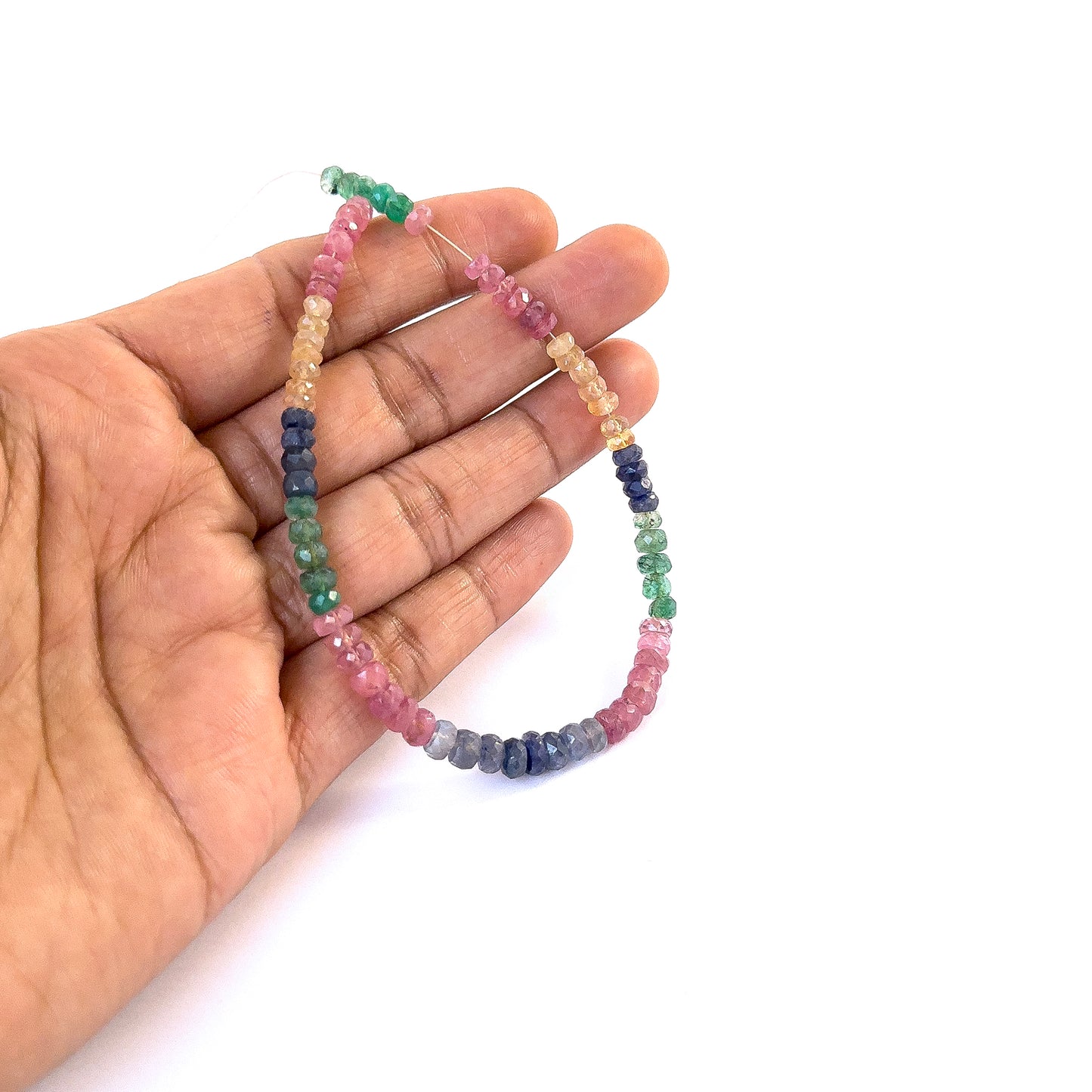 A person holds delicate strands of Ruby, Emerald and Sapphire faceted rondelle beads, showcasing their cut design.