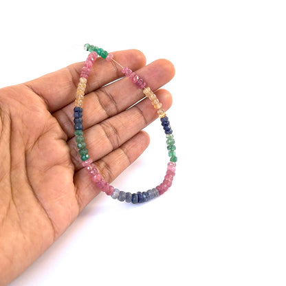 A person holds delicate strands of Ruby, Emerald and Sapphire faceted rondelle beads, showcasing their cut design.