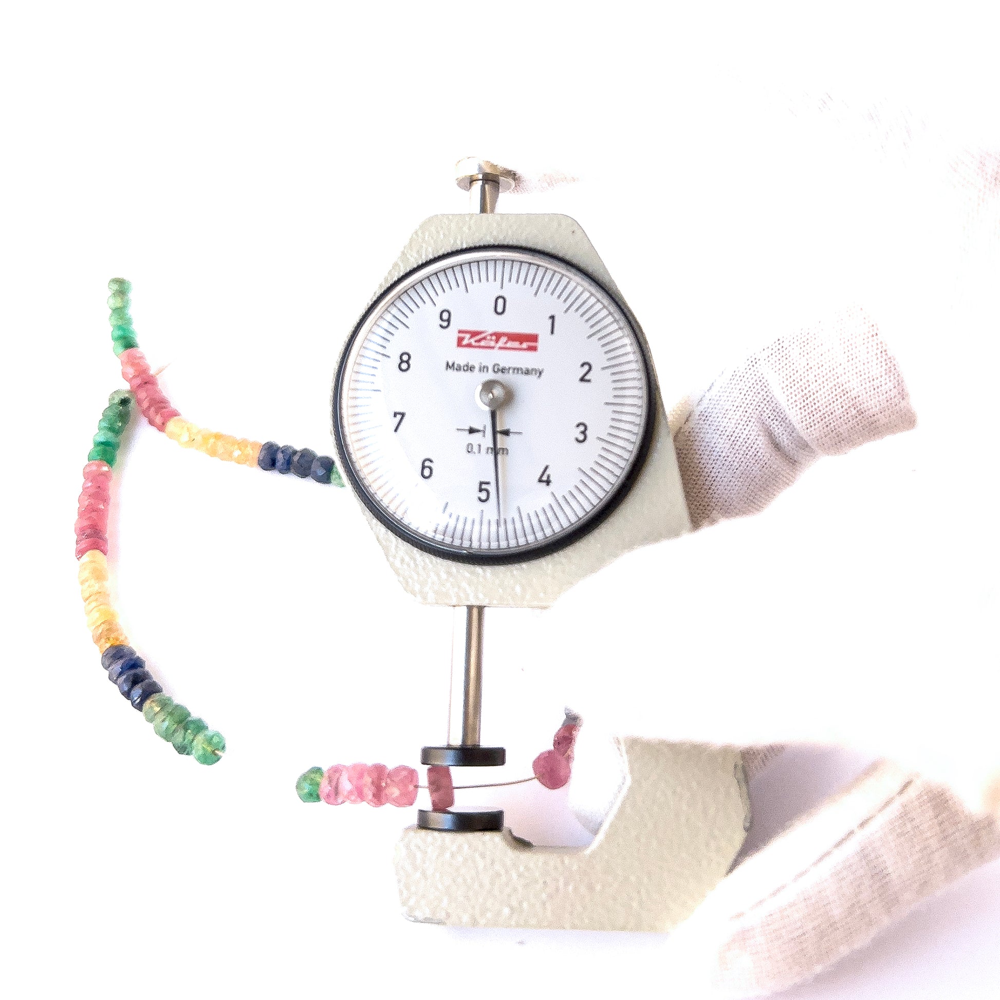 A dial gauge measures the Ruby, Emerald and Sapphire faceted rondelle 4.1–5mm gemstone.