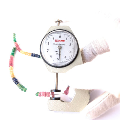 A dial gauge measures the Ruby, Emerald and Sapphire faceted rondelle 4.1–5mm gemstone.