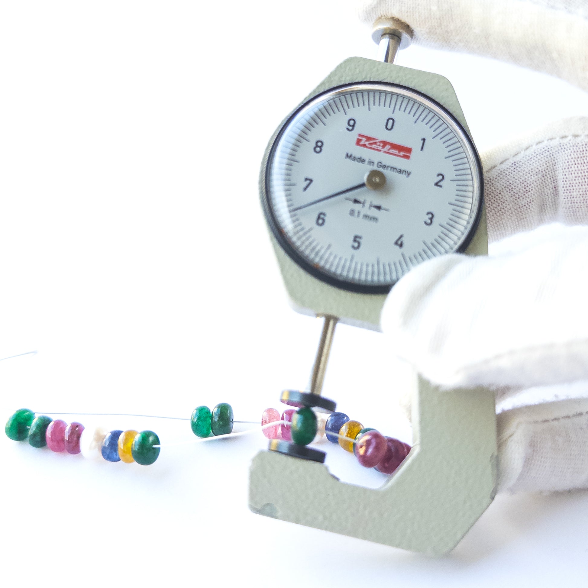A dial gauge measures the Ruby, Emerald, Sapphire and Pearl smooth rondelle 6.5mm gemstone.