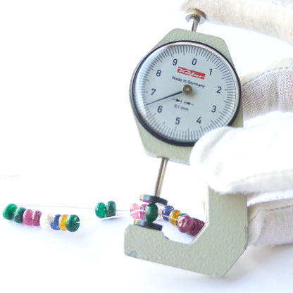 A dial gauge measures the Ruby, Emerald, Sapphire and Pearl smooth rondelle 6.5mm gemstone.