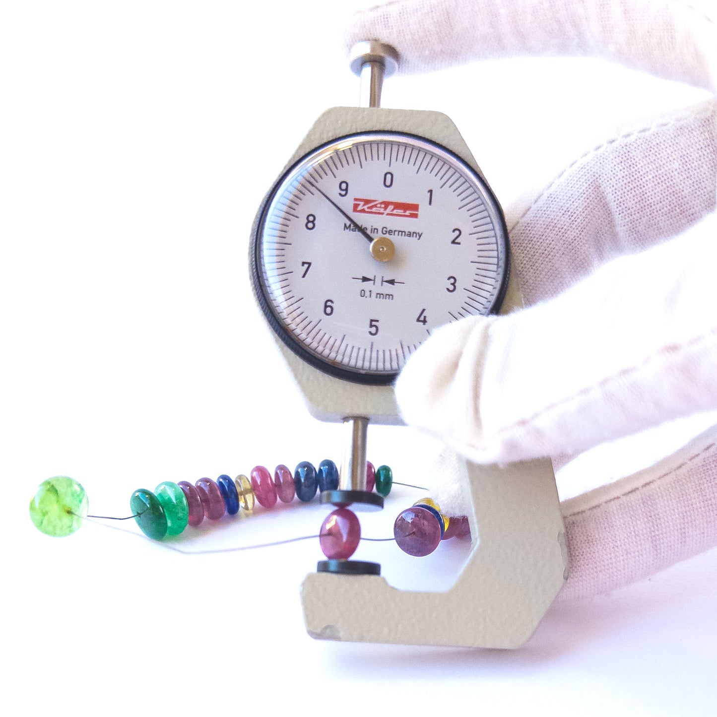 A dial gauge measures the Ruby, Emerald and Sapphire smooth rondelle 7.5–10mm gemstone.