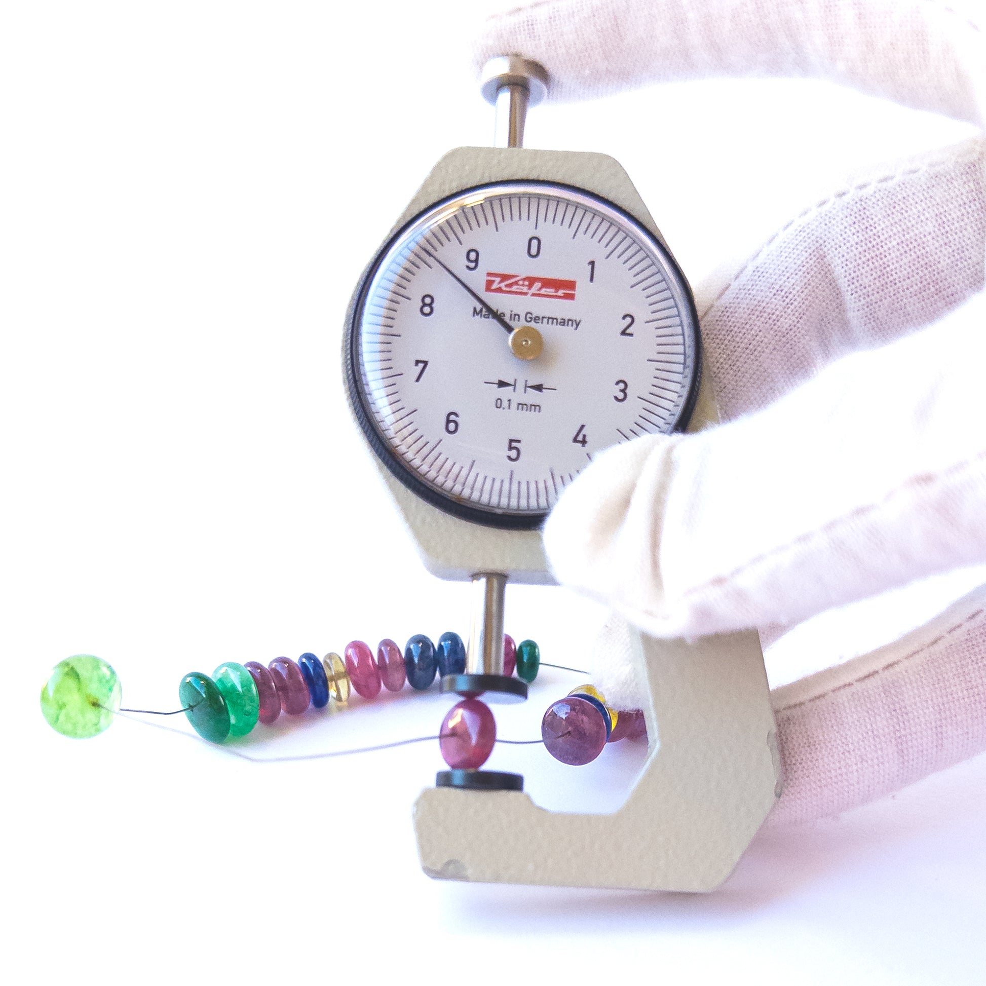 A dial gauge measures the Ruby, Emerald and Sapphire smooth rondelle 7.5–10mm gemstone.