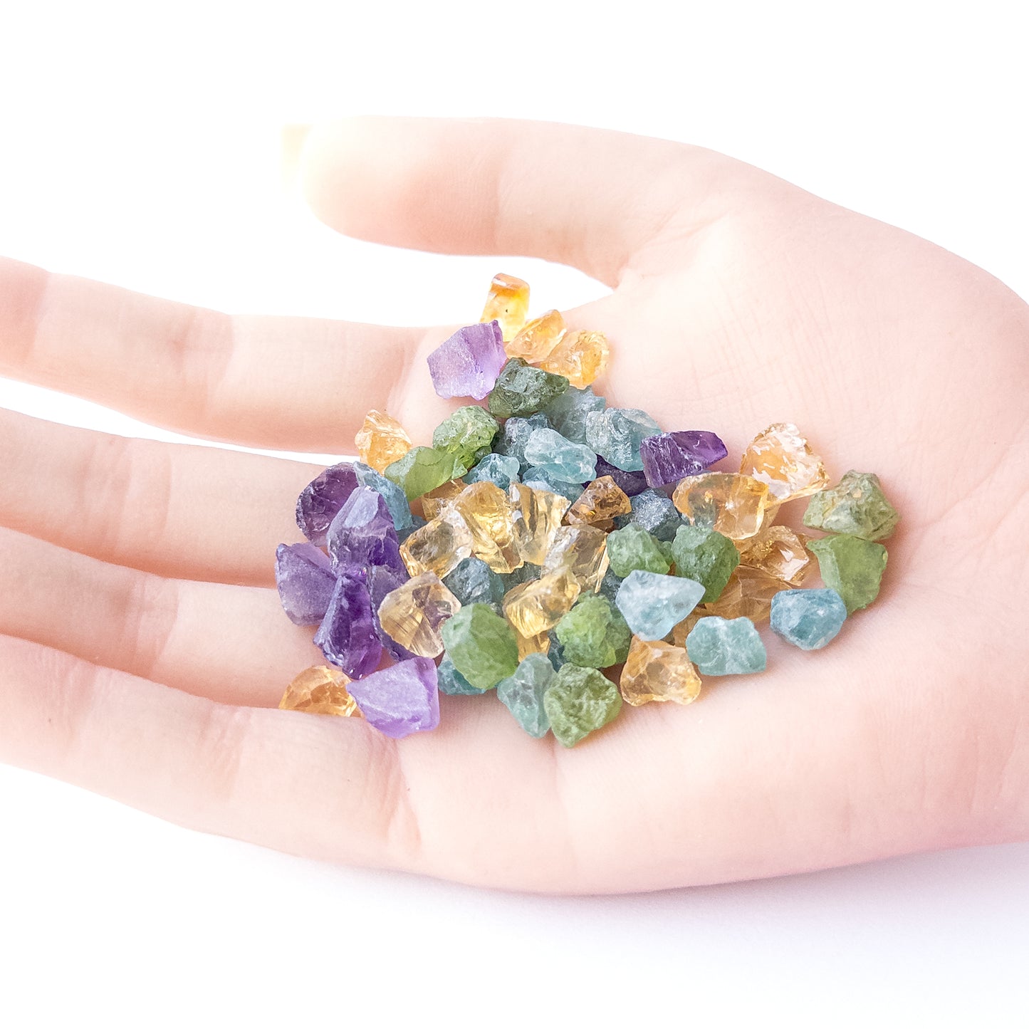 A person holds delicate pieces of Amethyst, Citrine, Apatite and Peridot rough, showcasing their natural design.