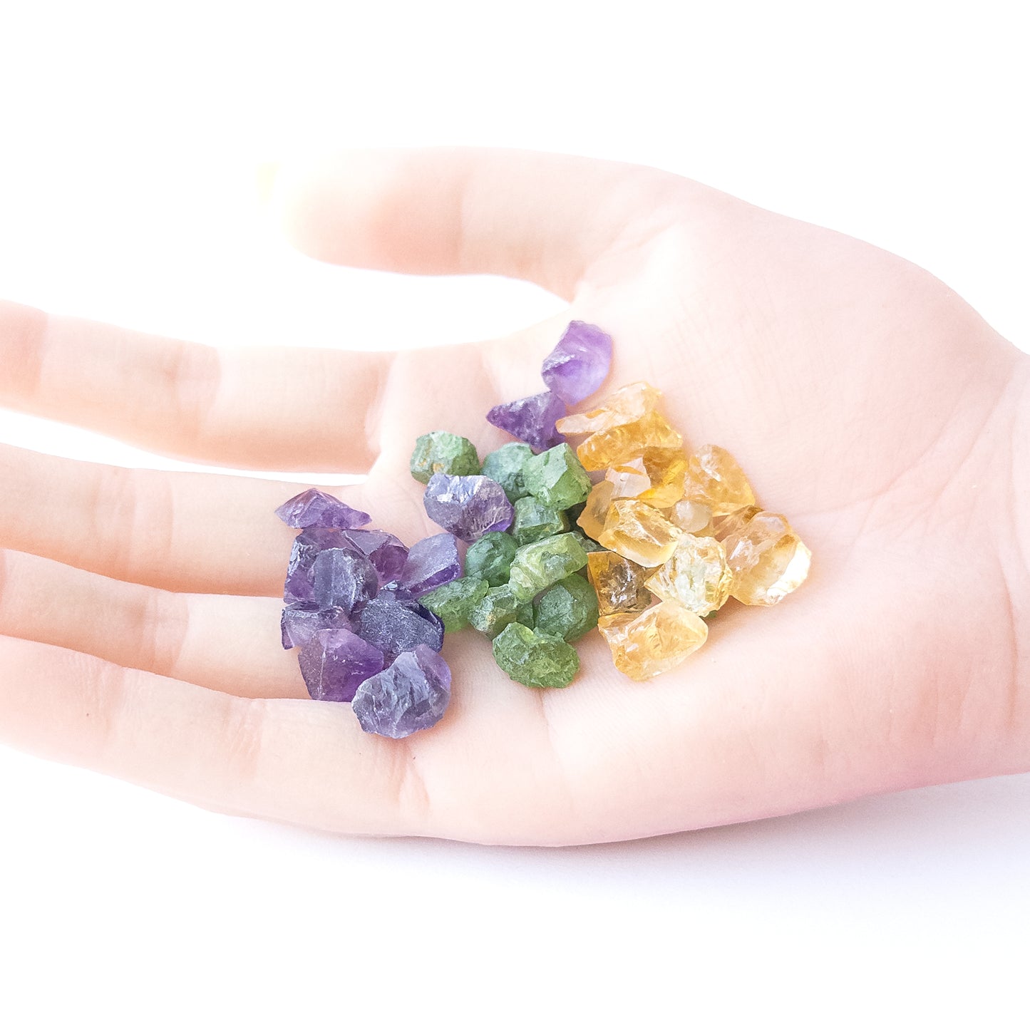 A person holds delicate pieces of Amethyst, Citrine and Peridot rough, showcasing their natural design.