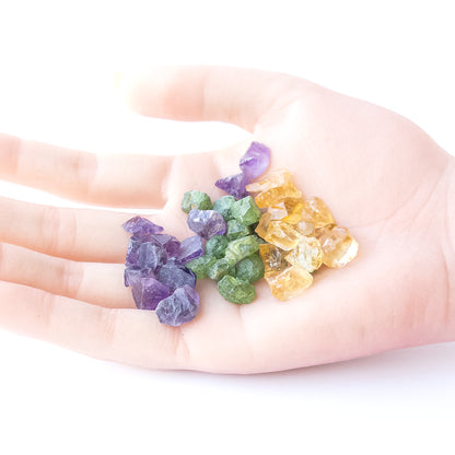 A person holds delicate pieces of Amethyst, Citrine and Peridot rough, showcasing their natural design.