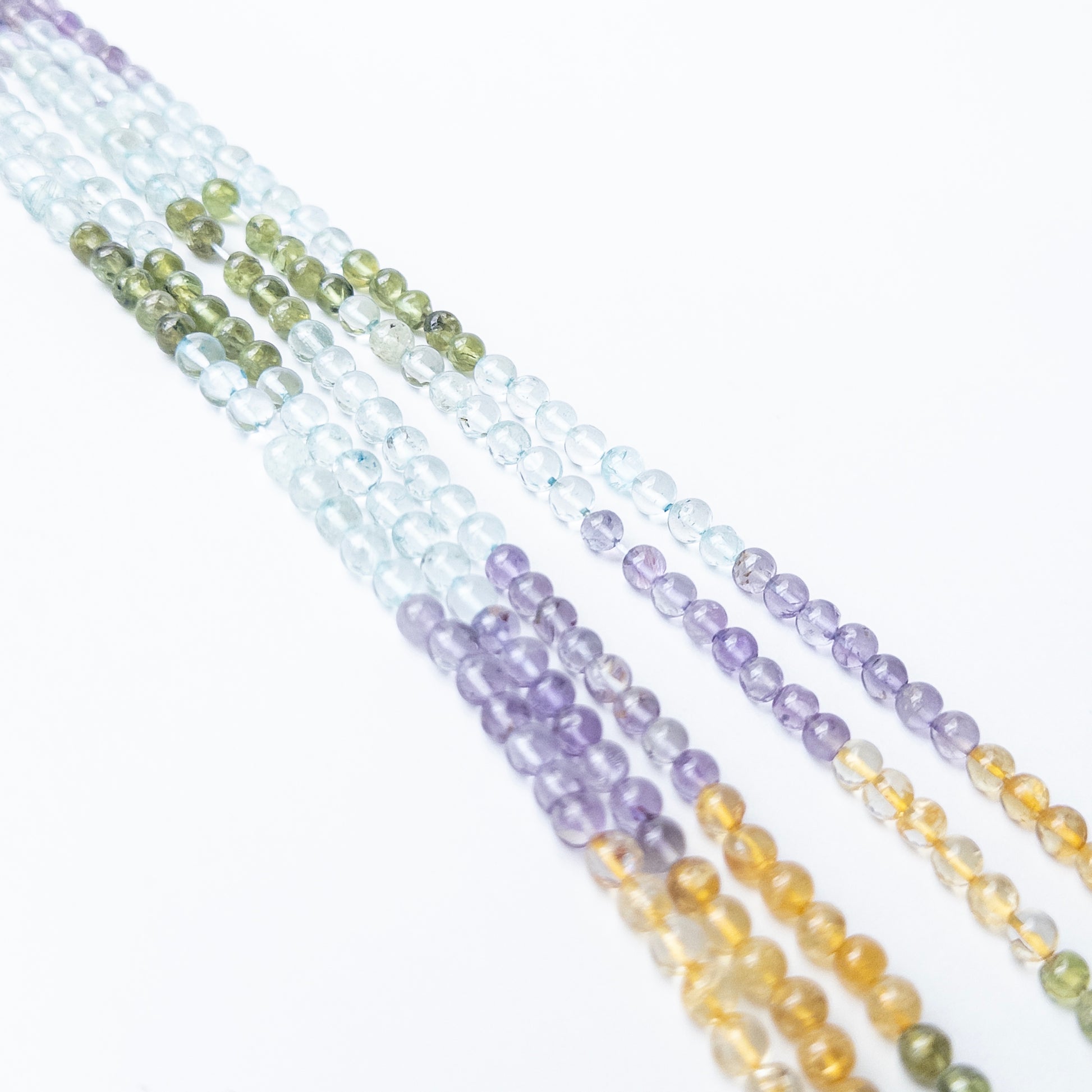 A person holds delicate strands of multi stone beads, showcasing their smooth round design.
