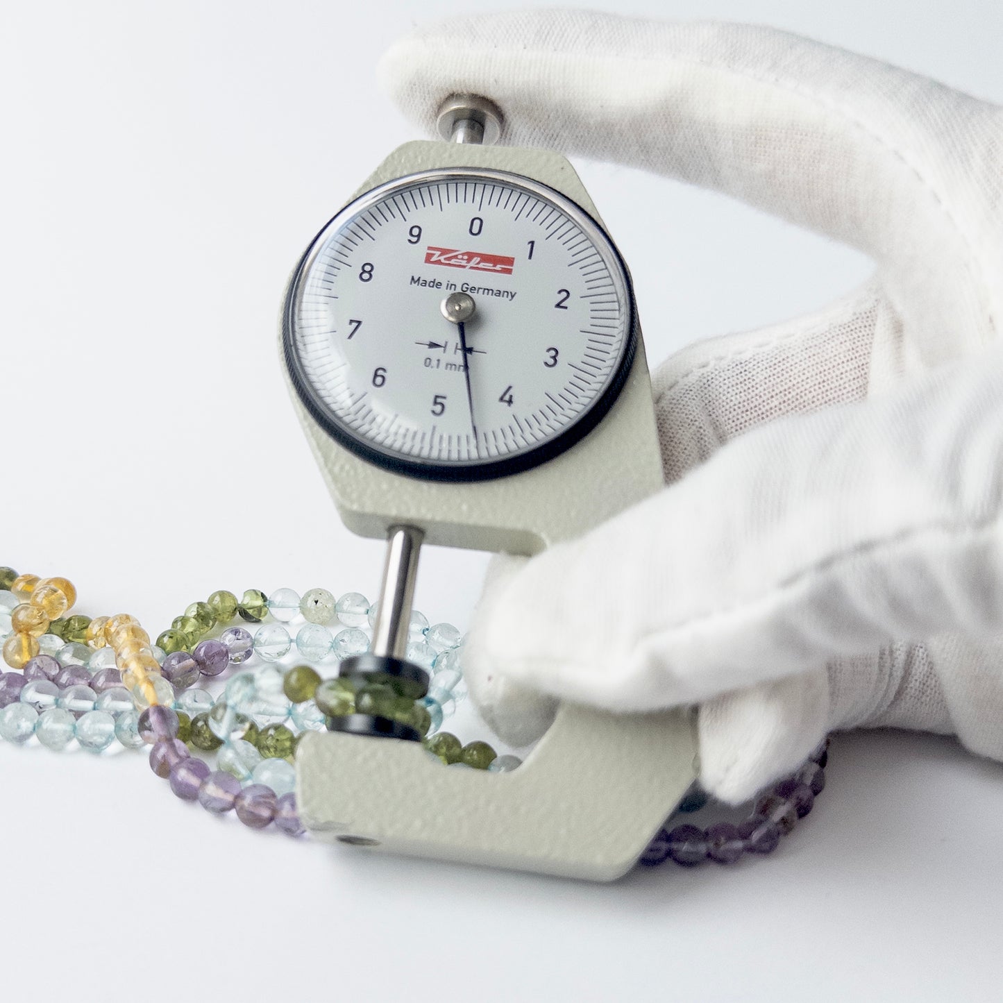 A dial gauge measures the multi stone smooth round 4.5–4.7mm gemstone.