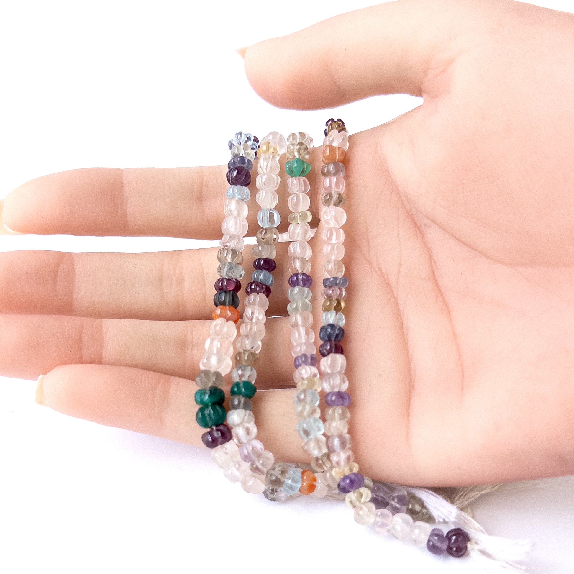 A person holds delicate strands of multi stone carved pumpkin beads, showcasing their carved design.