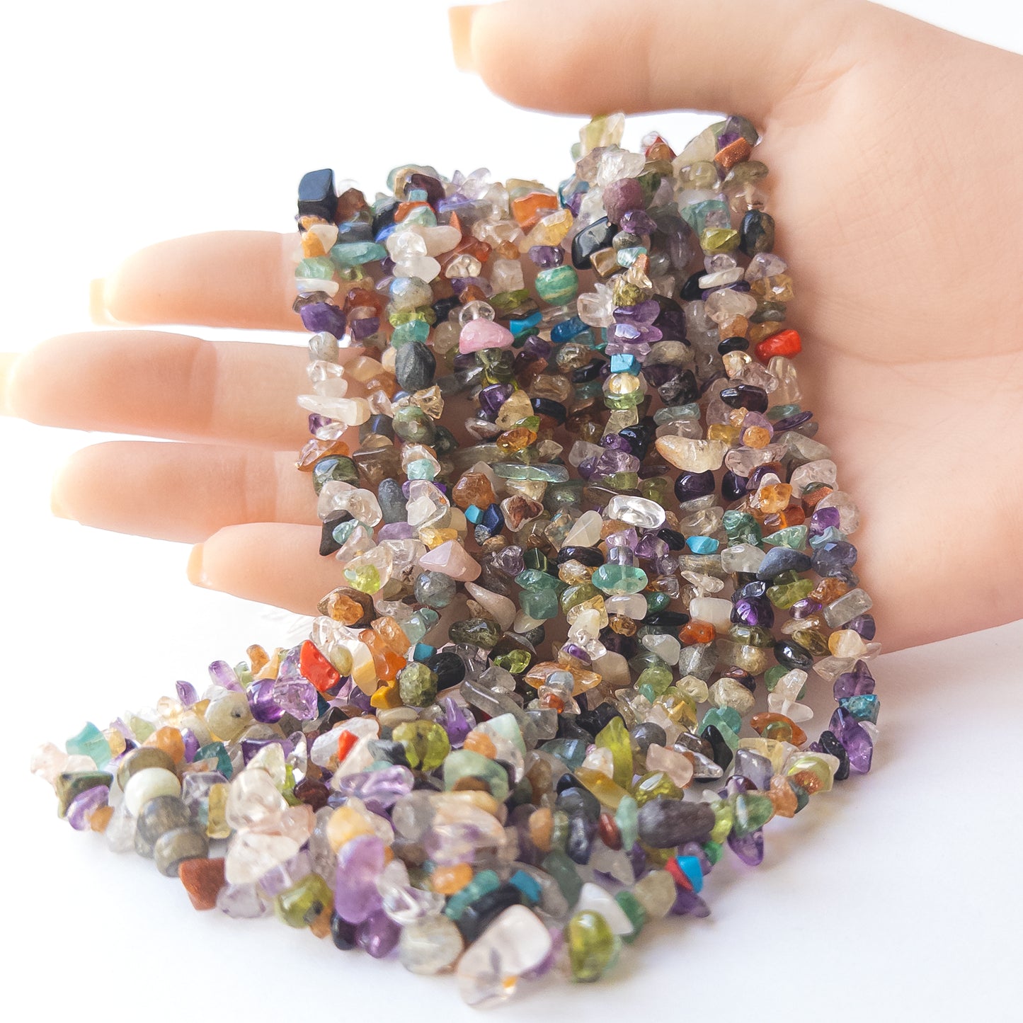 A person holds delicate strands of multi‑stone chip beads, showcasing their organic design.