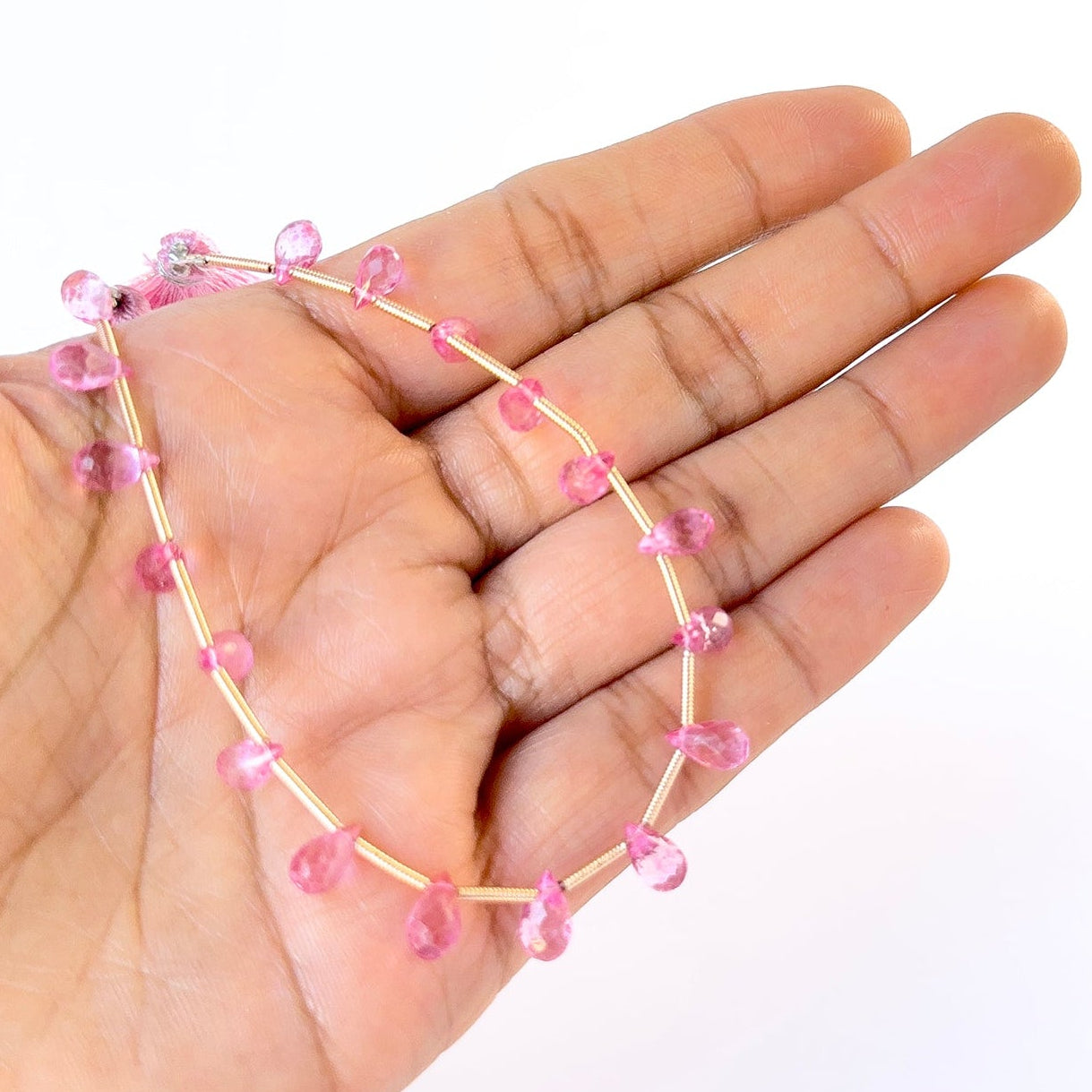 A person holds delicate strands of Pink Topaz beads, showcasing their faceted briolette design.