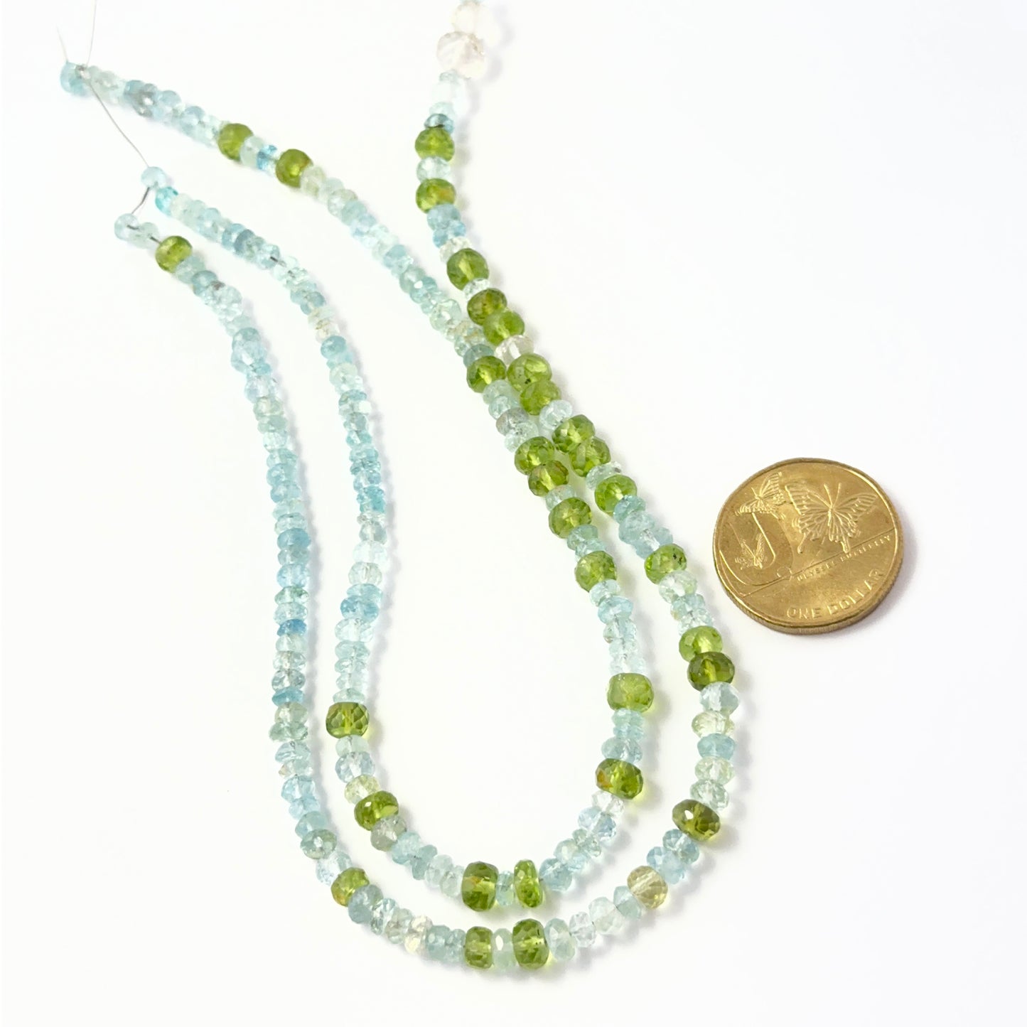 A coin is place near delicate strands of Peridot and Aquamarine beads for scale.