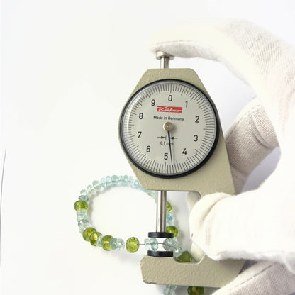 A dial gauge measures the Peridot and Aquamarine faceted rondelle 5–6mm gemstone