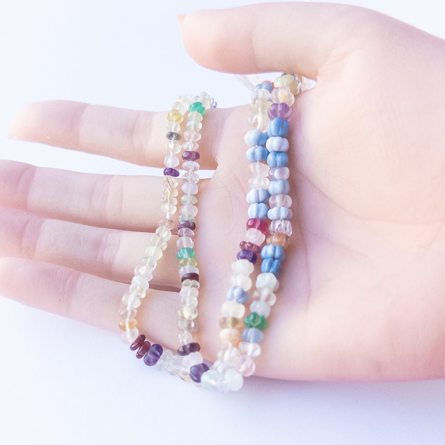 A person holds delicate strands of multi‑stone beads, showcasing their pumpkin cut design.