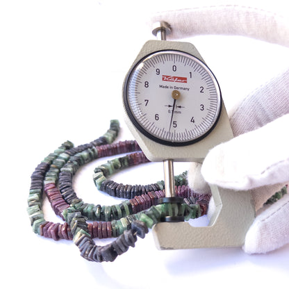 A dial gauge measures the Ruby, Sapphire and Emerald smooth square heishi 5.5mm gemstone.
