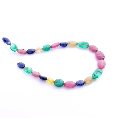 Close‑up of mixed ruby, blue sapphire and emerald smooth oval 6–7mm beads showing polished surfaces and vivid colour.