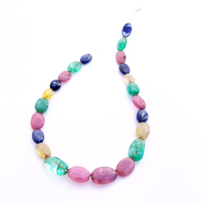 Smooth oval ruby, blue sapphire and emerald beads 6–7mm arranged to display uniform shape and rich gemstone hues.