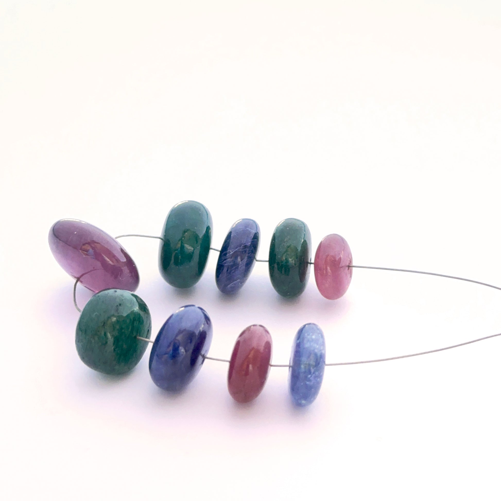 Close-up of mixed blue sapphire, ruby and emerald smooth rondelle beads showing polished surfaces and vivid hues.
