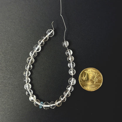 A coin is placed near delicate pieces of rose quartz and aquamarine beads for scale.