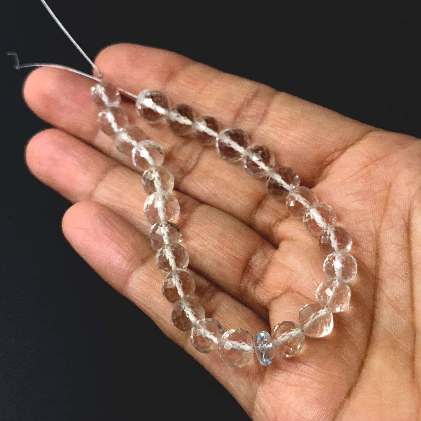 A person holds delicate strands of rose quartz and aquamarine beads, showcasing their faceted round design.