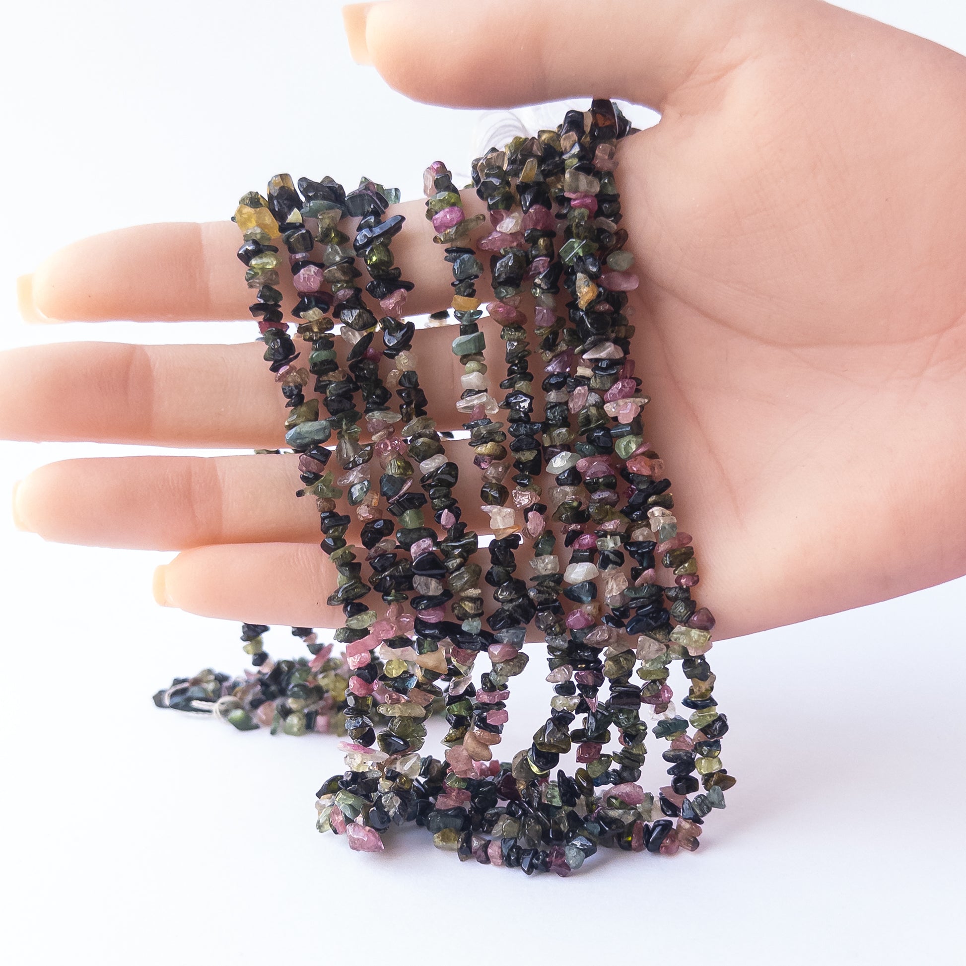 A person holds delicate strands of Multi Tourmaline beads, showcasing their chips and nuggets design.