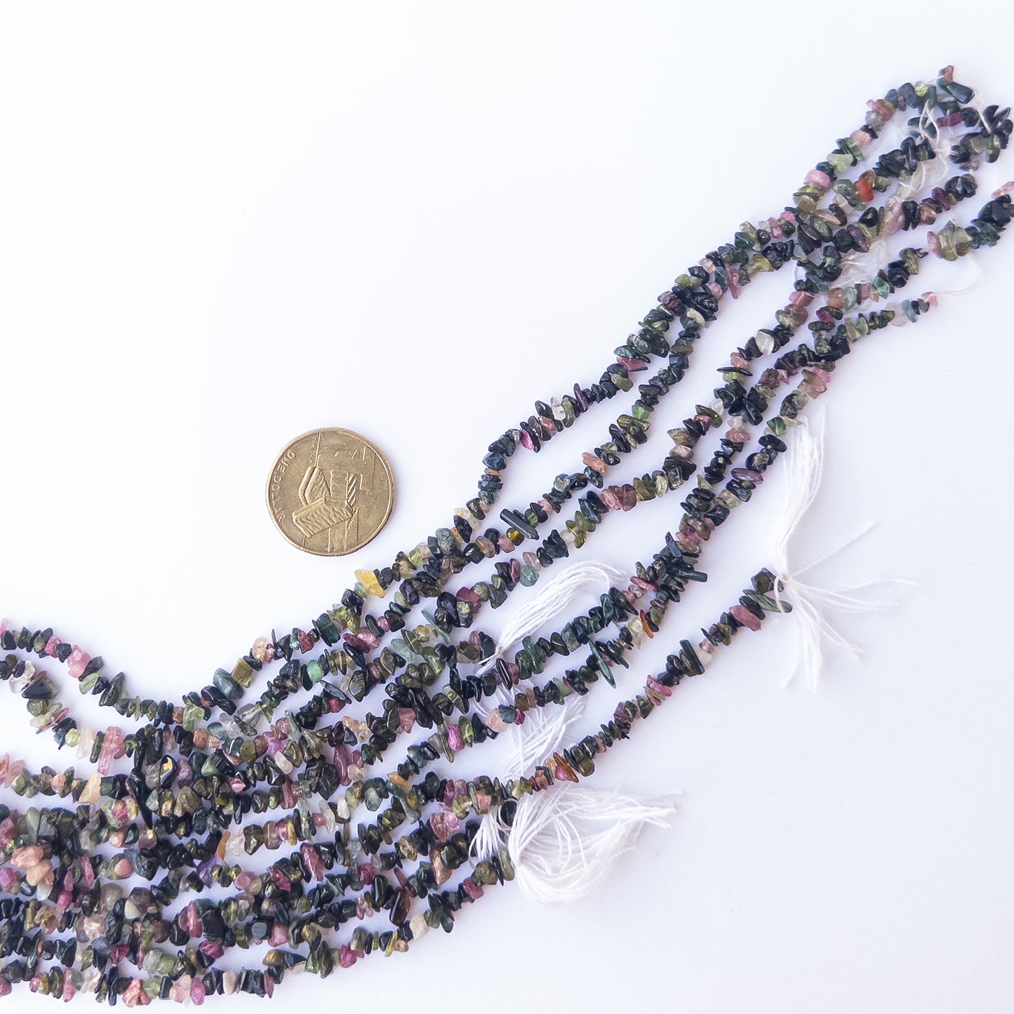 A coin is place near delicate strands of Multi Tourmaline beads for scale.