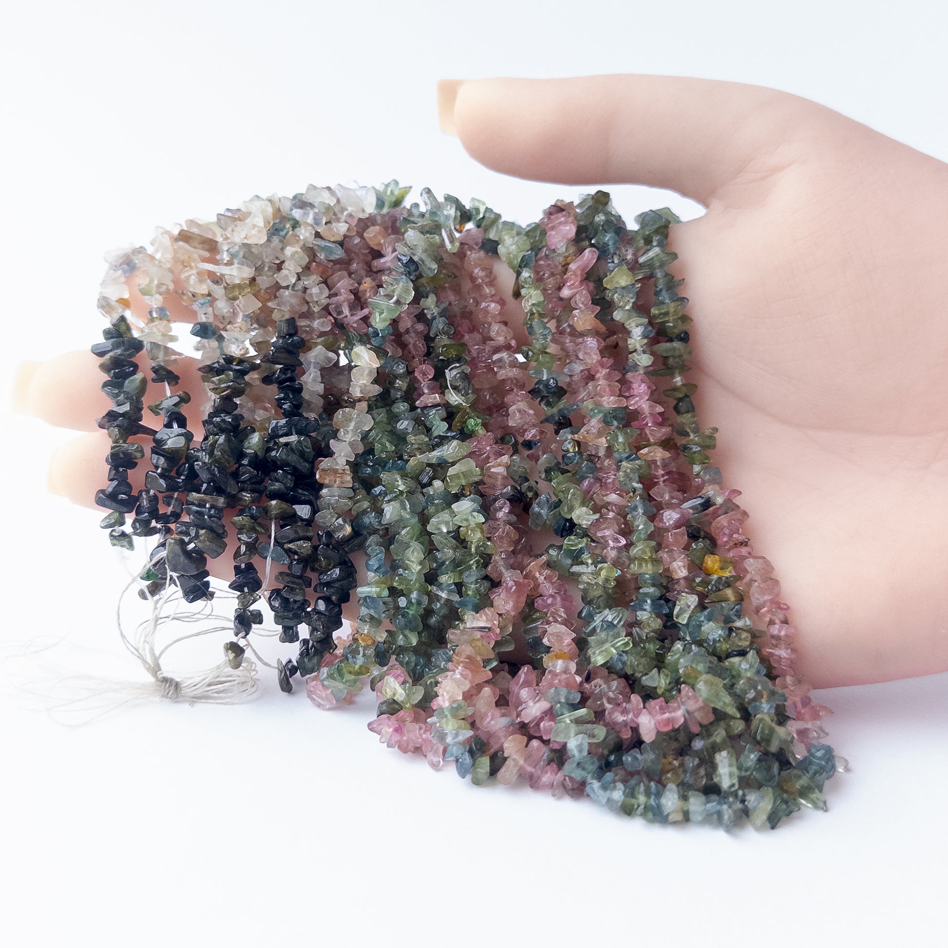 A person holds delicate strands of Multi Tourmaline beads, showcasing their chips and nuggets design.  
