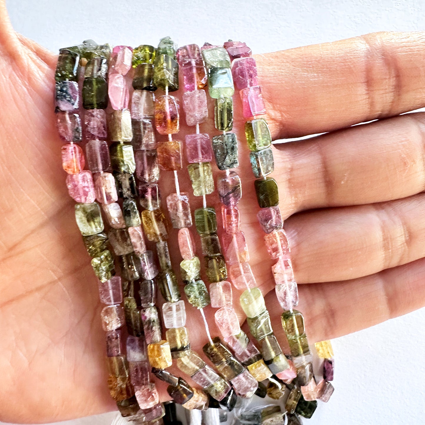 A person holds delicate strands of Multi Tourmaline beads, showcasing their smooth design.