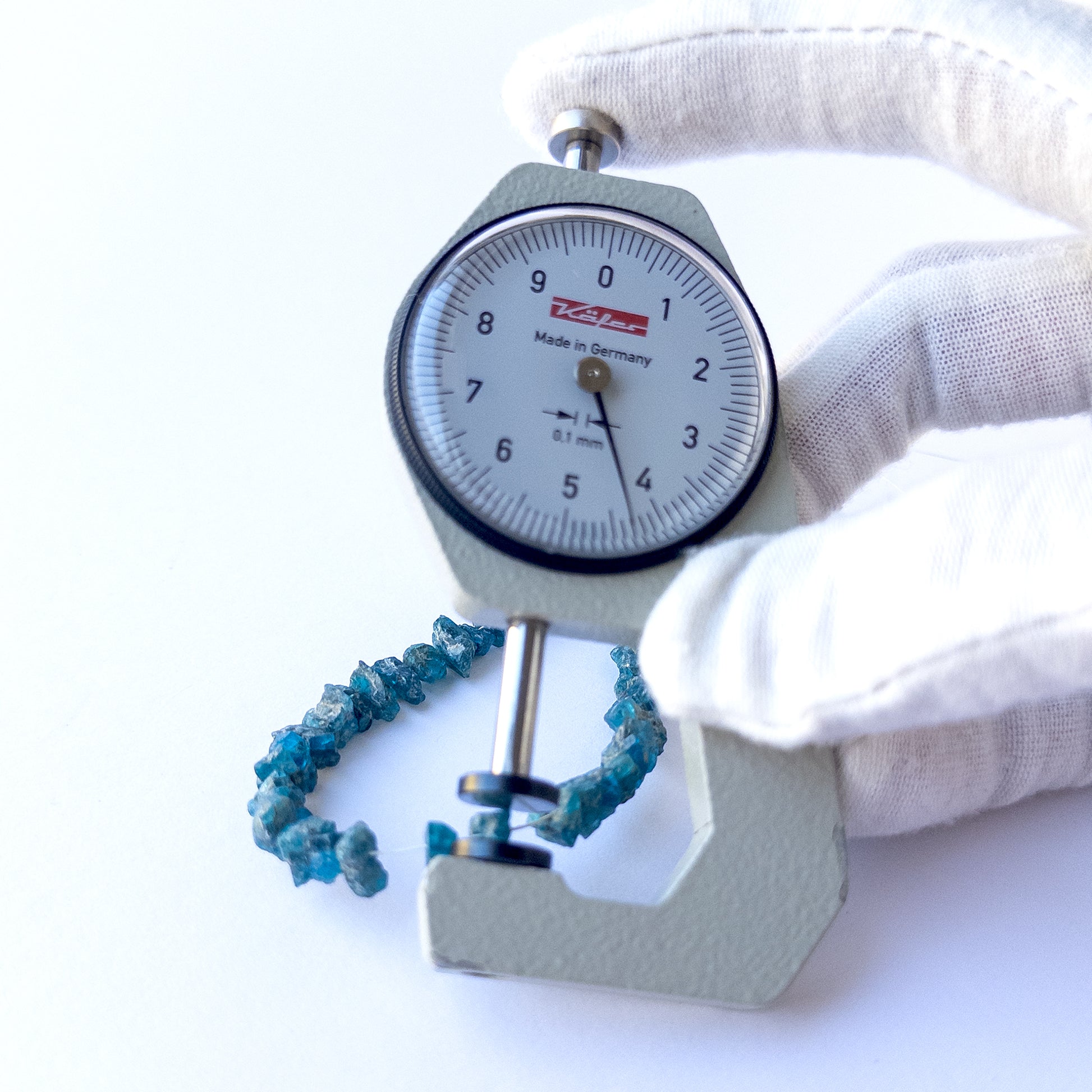 A dial gauge measures the Neon Apatite drilled rough 5–6mm gemstone.