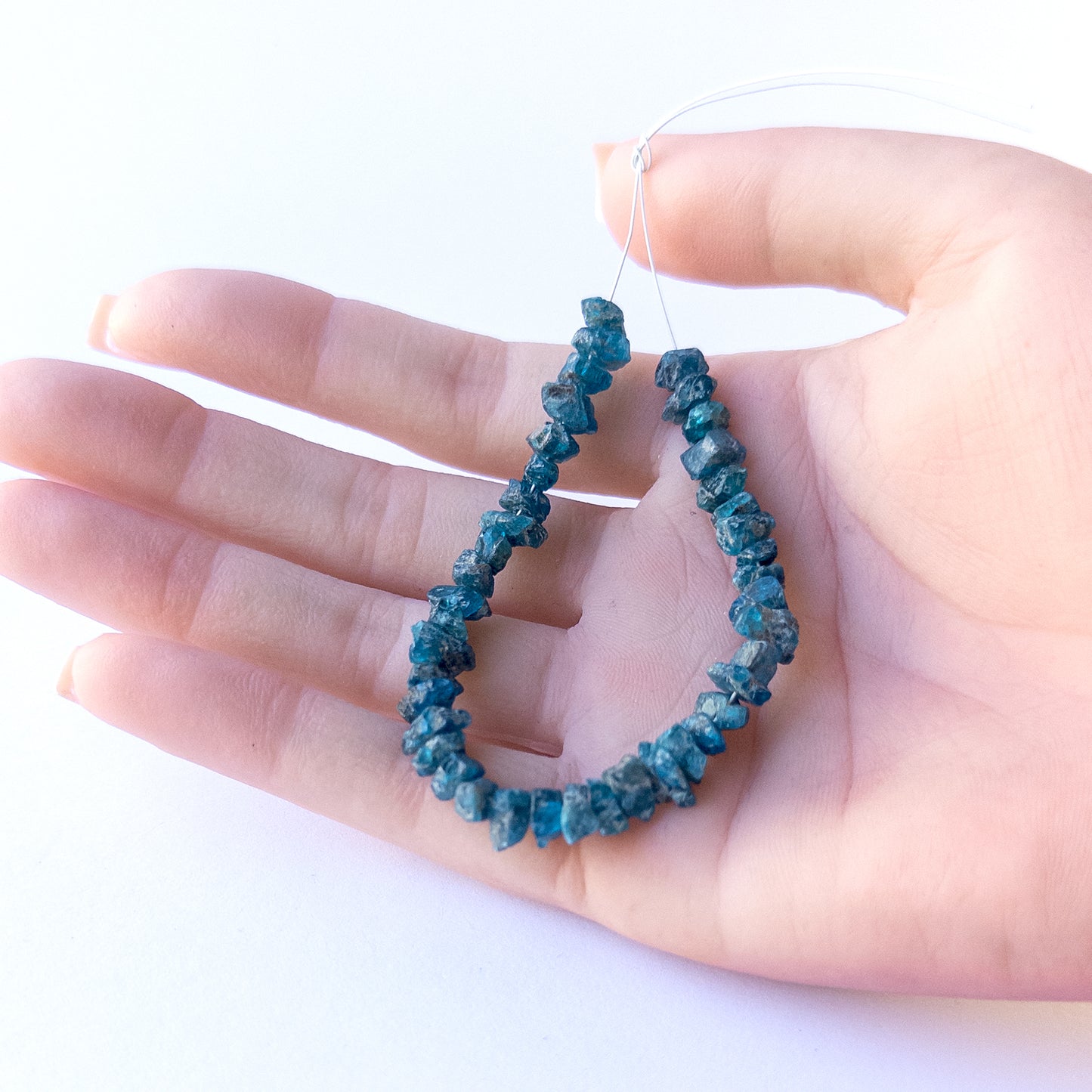 A person holds delicate strands of Neon Apatite drilled rough beads, showcasing their natural rough design.