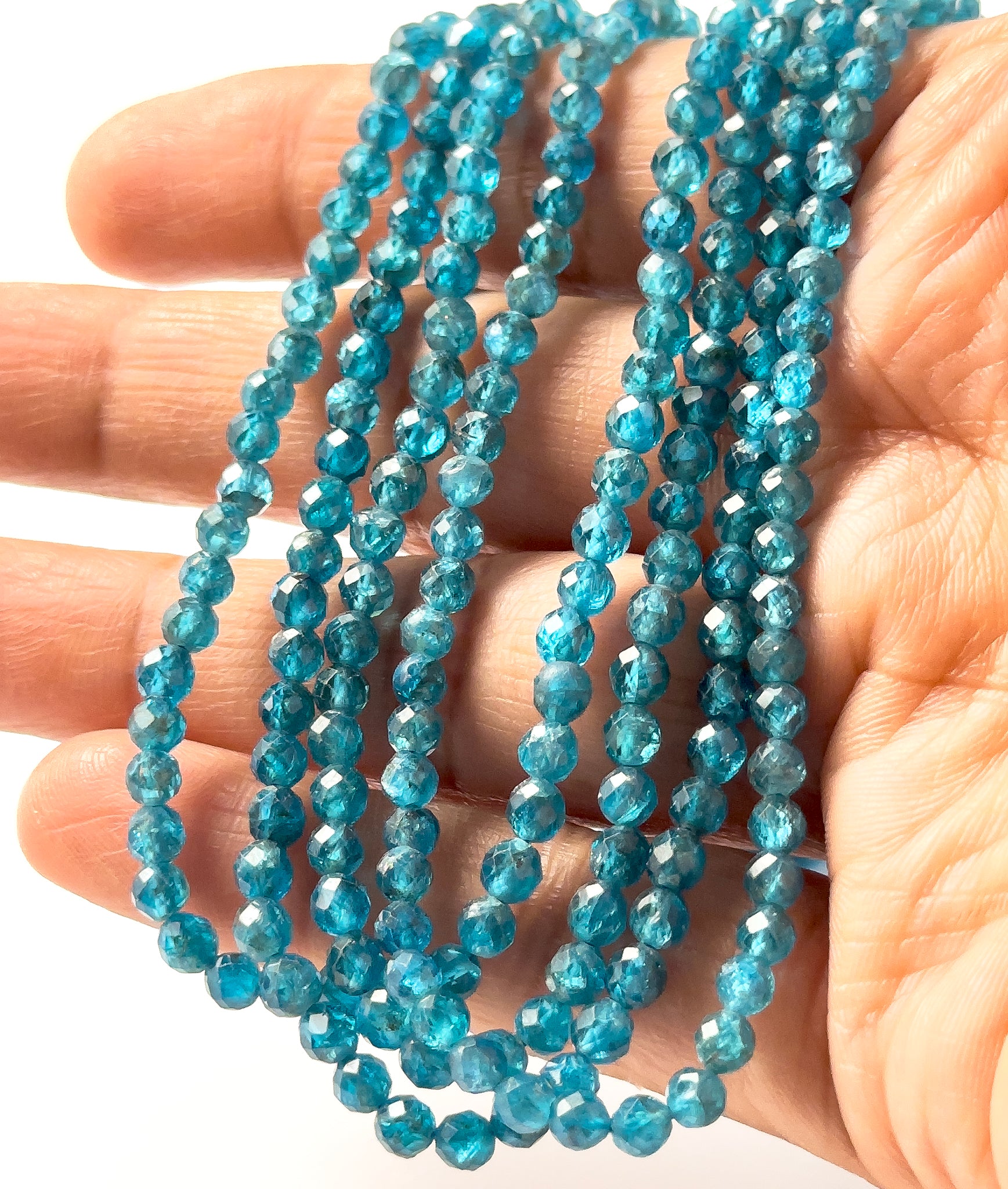 A person holds Neon Apatite rondelle beads, showing their faceted design and vivid blue colour.