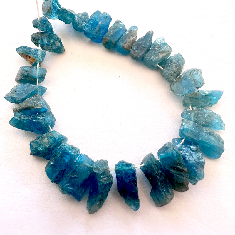 Uncut Neon Apatite beads showing electric blue hues and organic finish.