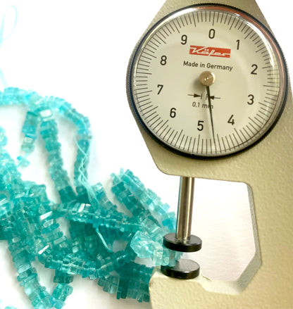A dial gauge measures the Neon Apatite smooth square heishi 4.5–5.5mm gemstone.