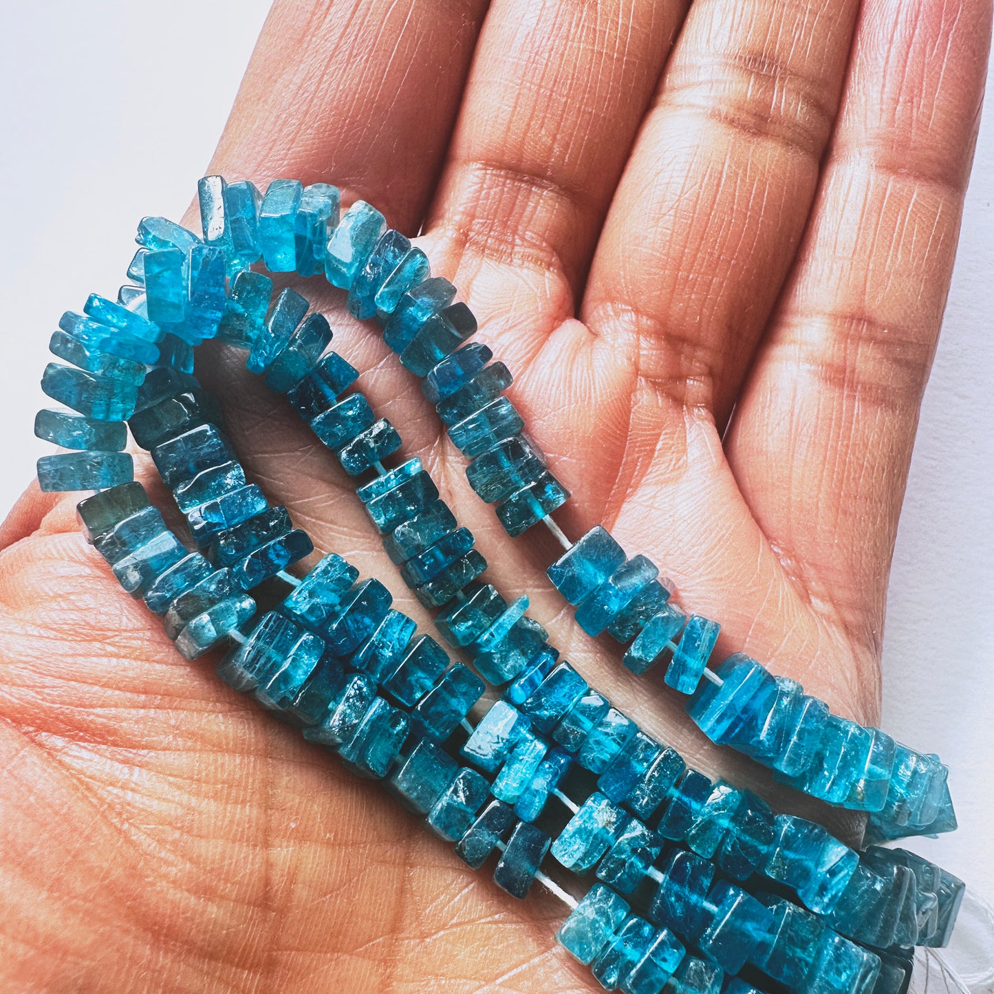 A person holds delicate strands of Neon Apatite beads, showcasing their smooth design.