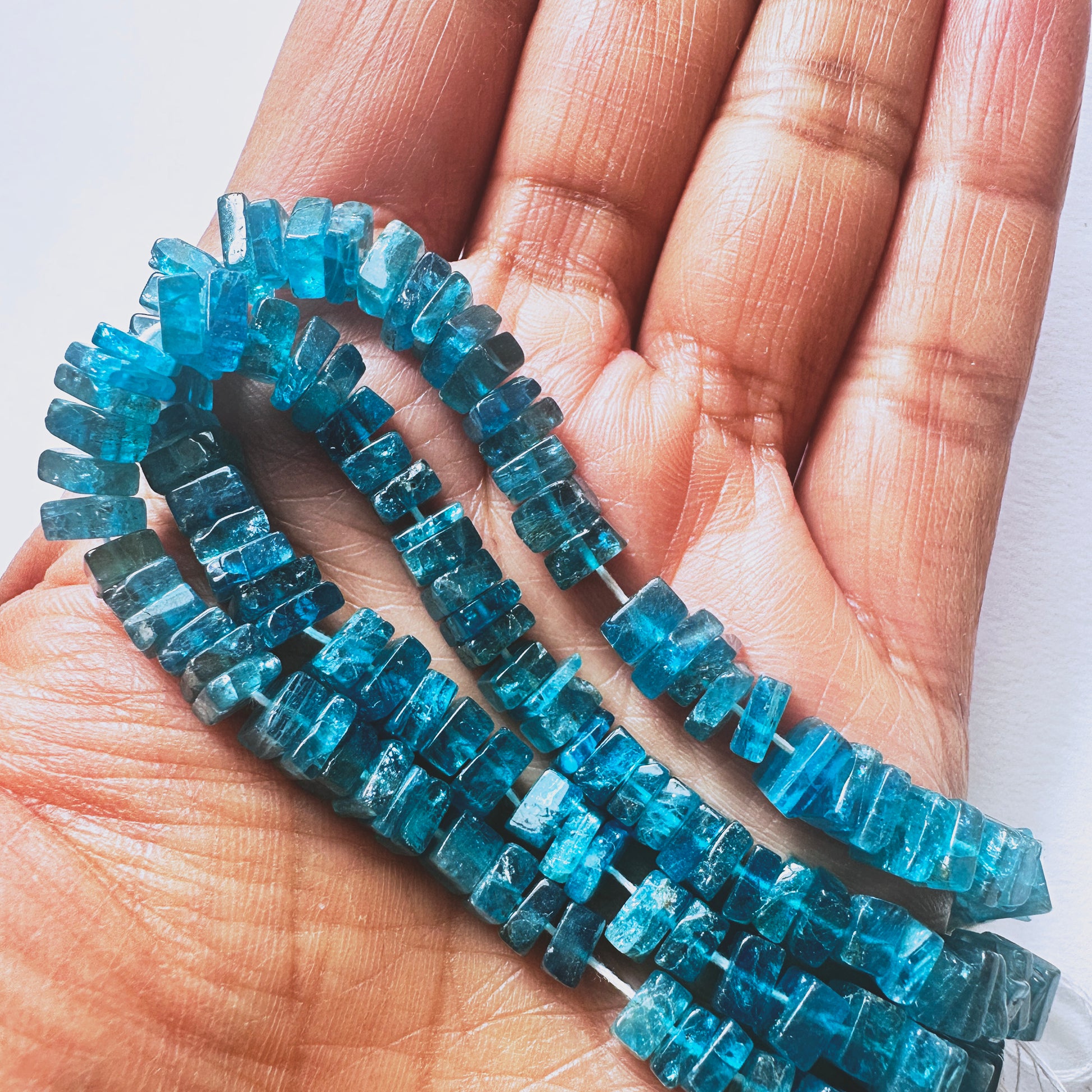 A person holds delicate strands of Neon Apatite beads, showcasing their smooth design.